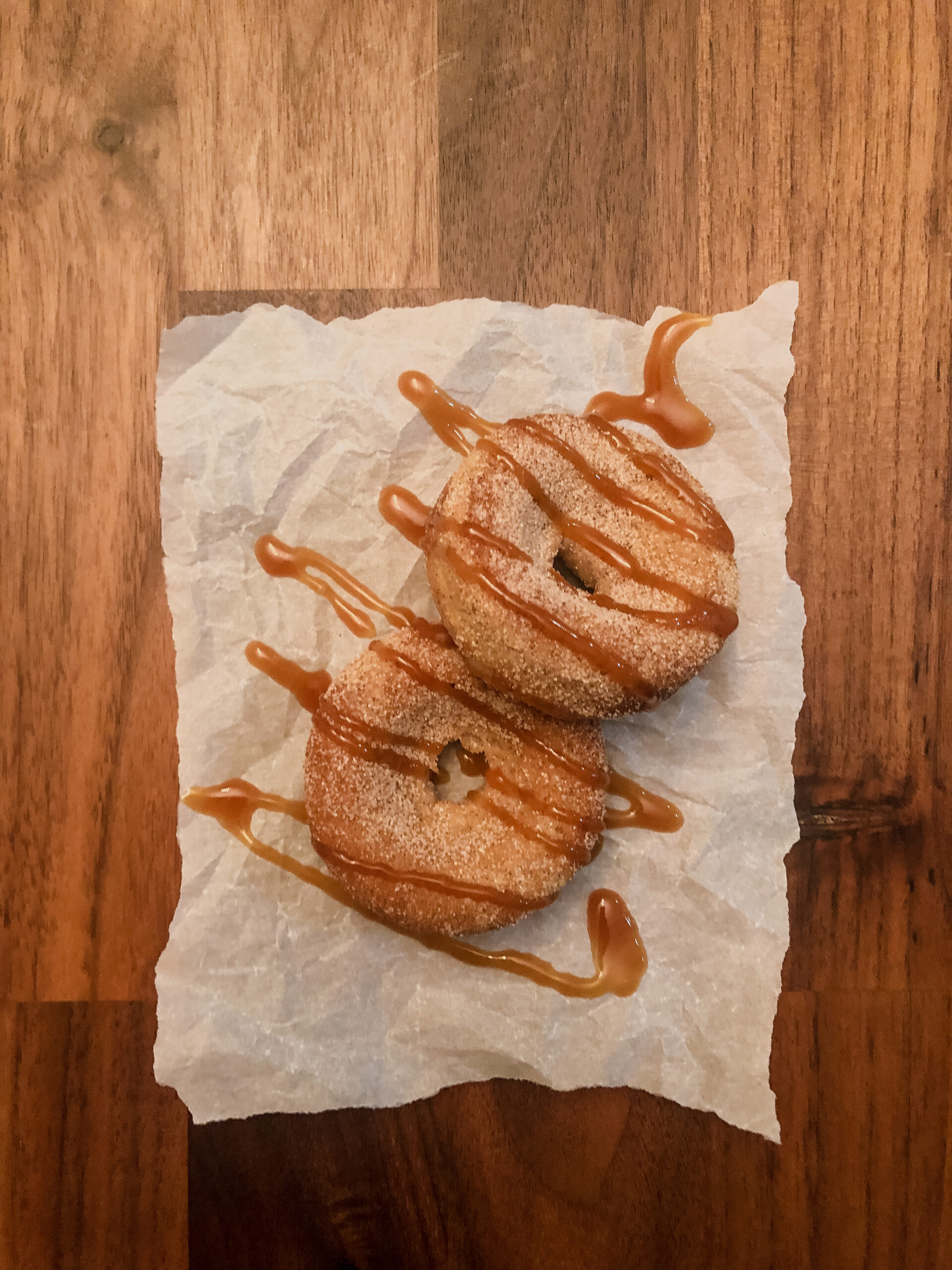 Gluten free cinnamon sugar donuts drizzled with salted caramel laying on parchment paper