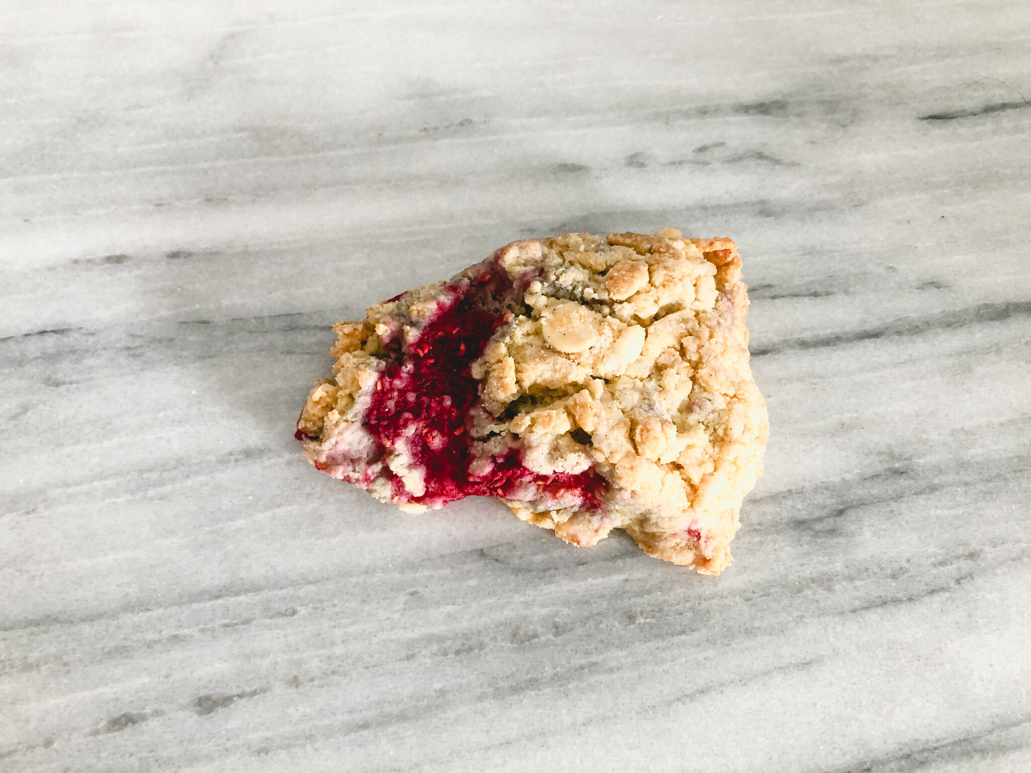 Single gluten free white chocolate raspberry scone on a marble table
